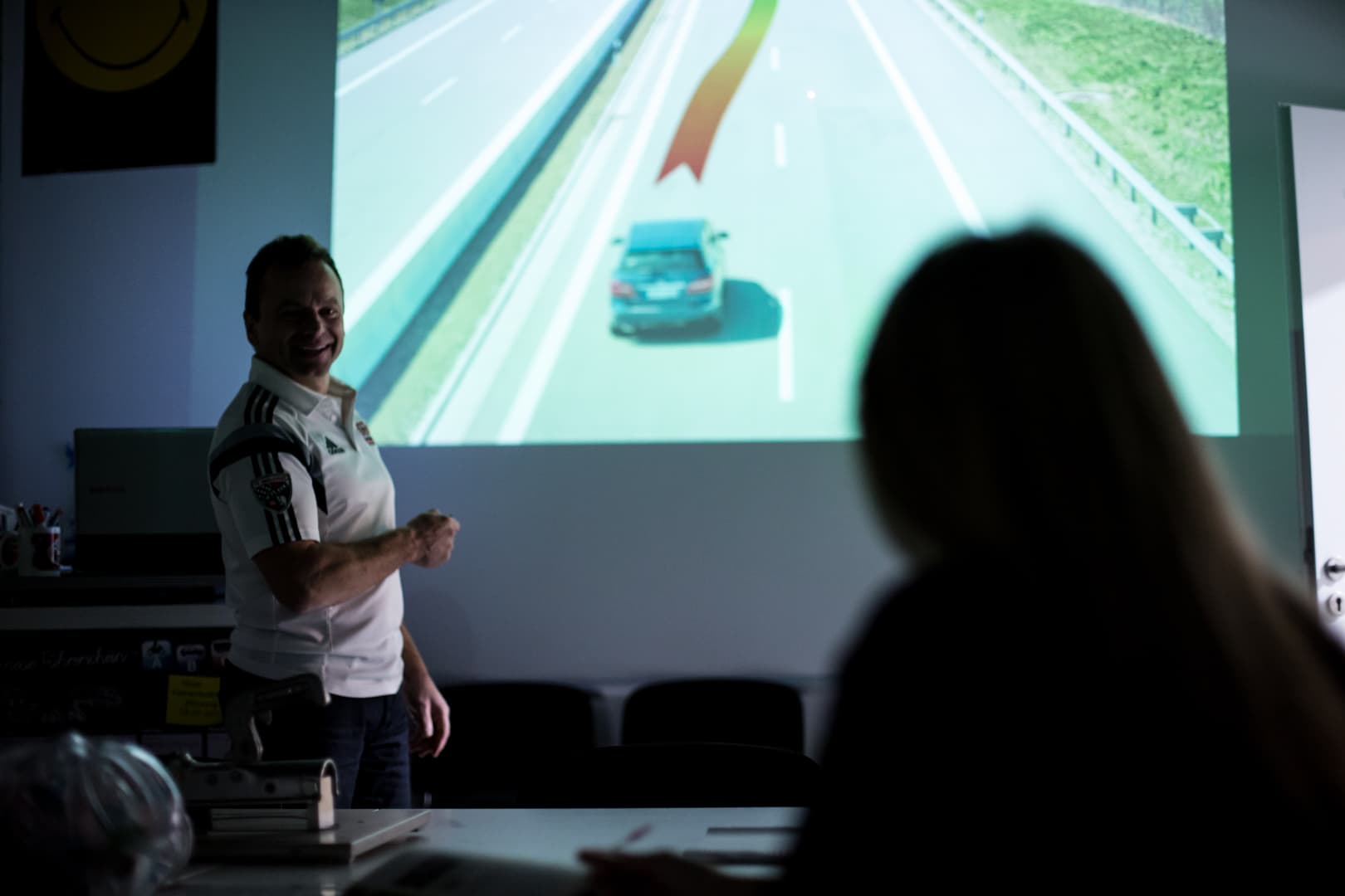 Fahrlehrer im Theorieunterricht vor einer Verkehrssituation an der Wand